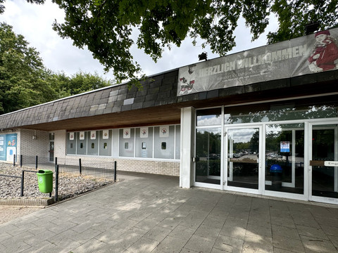 Eissporthalle  Eingang eines Gebäudes mit Glasfront, weißer Ziegelfassade und einem Banner am Dachvorsprung.