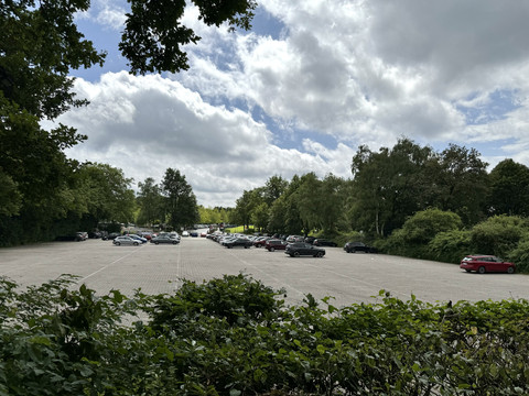 Eissporthalle Parkplatz Großer Parkplatz im Grünen, umgeben von Bäumen und Sträuchern. Einige Autos parken dort.