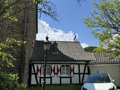 Burghaus Scheltensülz Fachwerkhaus mit roten Fensterläden, Wetterhahn auf dem Dach; blauer Himmel und ein parkendes Auto vorne.