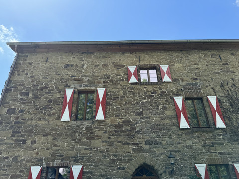 Burghaus Scheltensülz Historisches Steinhaus mit roten Fensterläden vor blauem Himmel, robust und charmant im Stil.