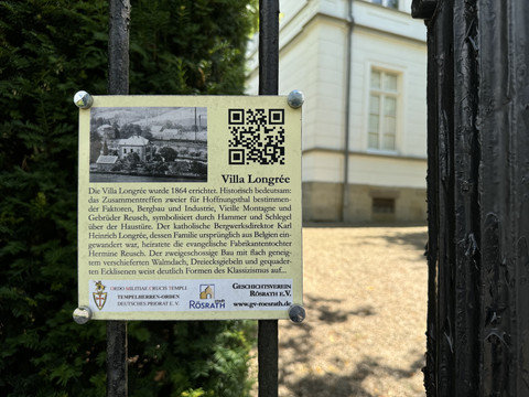 Villa Longrée - Infoschild Schwarz-weiße Infotafel über die historische Villa Longrée, befestigt an einem geschmiedeten Gitter.