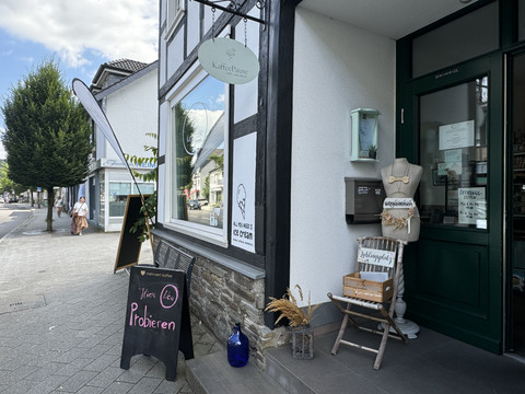 Kaffeepause - Außenansicht <p>Eingang eines Cafés mit Schaufenster, Dekoration und Aufstellschildern auf Bürgersteig.</p>