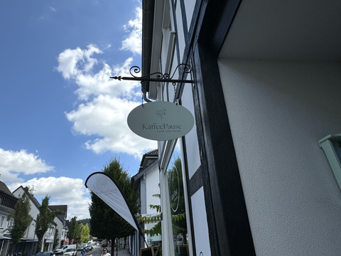 Kaffeepause - Ansicht Schild KaffeePause Café-Schild an einem Fachwerkgebäude bei sonnigem Wetter, Menschen spazieren darunter.