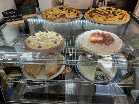 Kaffeepause - Ansicht Kuchenauslage Vier verschiedene Kuchen und eine Quiche in einer beleuchteten Glasvitrine.