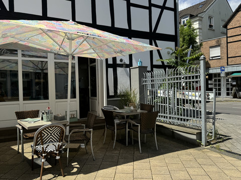 Kaffeepause - Ansicht Außenterrasse Gemütliche Außenterrasse eines Cafés mit buntem Sonnenschirm und modernen Rattanmöbeln.