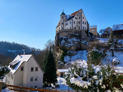 Burg Hohnstein thront majestätisch auf einem schneebedeckten Felsvorsprung unter klarem Winterhimmel.