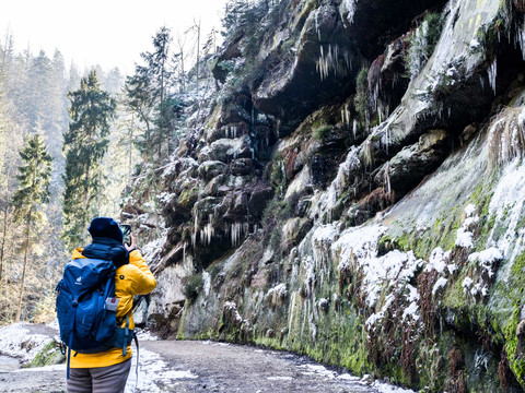 Wanderer im Winter durch das verschneite Polenztal, umgeben von vereisten Felsen und Tannen.