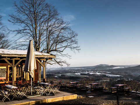 Terrasse einer Berghütte im Winter mit leeren Tischen und Stühlen; Schnee bedeckt die Landschaft.