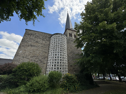 Kirche St. Walburga Kirche mit spitzem Turm und markanter Ziegelmauer, umgeben von grünen Bäumen und blauem Himmel.