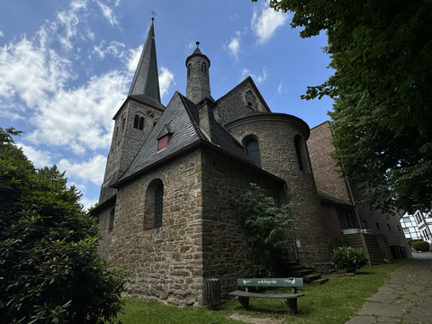 Kirche St. Walburga Historische Steinkirche mit Turm und Rundapsis, umgeben von Bäumen unter blauem Himmel.