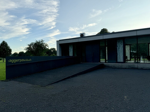 Gut Eichtal Modernes flaches Gebäude mit Glasfronten, umgeben von Bäumen und Grünfläche unter blauem Himmel.