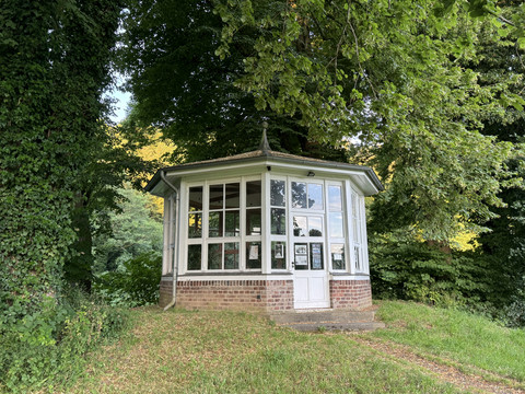 Gut Eichtal Historischer Pavillon aus Backstein und Glasfenstern, idyllisch von Bäumen umgeben, in grüner Landschaft.