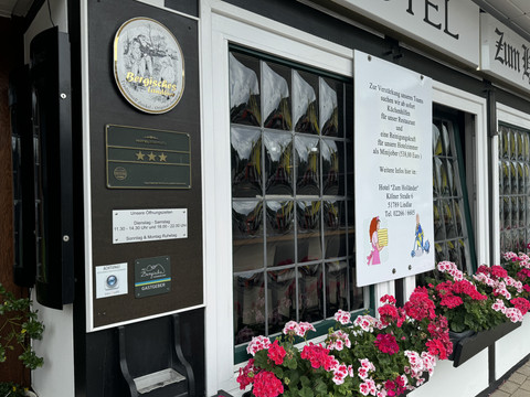 Hotel-Restaurant Zum Holländer - Außenansicht Die Front eines Hotels mit Schildern und blühenden Geranien vor einem Fenster.