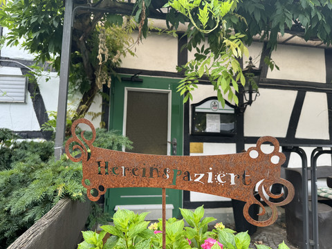 Gasthof Zum Stausee Rostige Metallschild mit der Aufschrift "Hereinspaziert" vor einem gemütlichen Fachwerkhaus.
