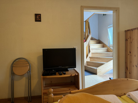 Gasthof Zum Stausee Ein Zimmer mit einem Holz-Bett, TV auf Holz-Tisch und einer Treppe im Hintergrund, schlicht eingerichtet.