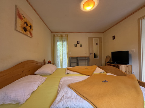 Gasthof Zum Stausee Gemütliches Schlafzimmer mit Doppelbett, gelber Bettwäsche, warmem Licht und Flachbildfernseher.