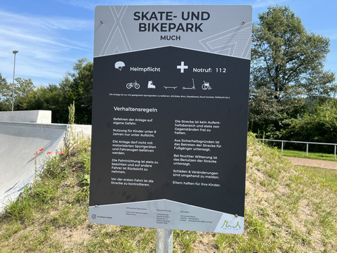 Skaterpark Much Skate- und Bikepark-Schild in Much mit Verhaltensregeln und Helmpflicht unter blauem Himmel.