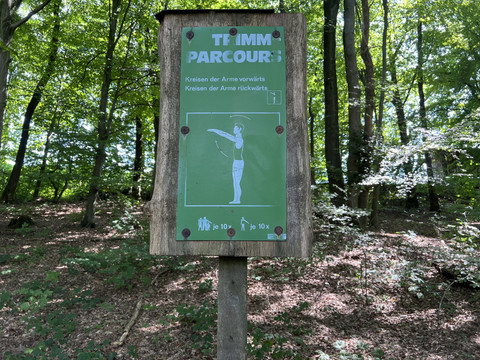 Trimm-Dich-Pfad  <p>Holzschild im Wald mit Beschreibung einer Armübung für einen Trimm-Parcours.</p>