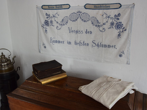 Bauernhofmuseum Alte Holztruhe mit Büchern und Leinentuch, Wandstickerei: "Vergiss den Kummer im tiefsten Schlummer".