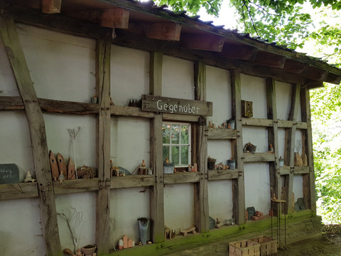 Galerie Sattelgut Fachwerkhausfassade mit kleinen Töpferwaren und Schildern, umgeben von schattigen Bäumen.