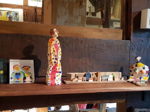 Galerie Sattelgut Eine bunte Sammlung von bemalten Holz- und Tonfiguren auf einem rustikalen Holzregal in warmer Umgebung.