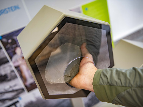 Bergisches Grauwacke-Museum Hand greift durch hexagonale Öffnung auf Museumsobjekt; interaktive Erfahrung in moderner Ausstellung.