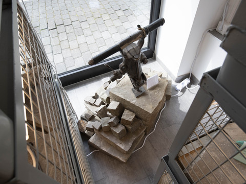 Bergisches Grauwackemuseum Steinhammer auf Steinsockel, umgeben von Pflastersteinen, in modernem Ausstellungsraum mit Glasfenster.