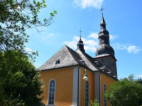 Evangelische Barockkirche Eckenhagen Barockkirche mit Zwiebeltürmen vor blauem Himmel, umgeben von grünen Bäumen und Laterne im Vordergrund.