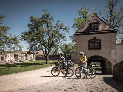Kasteel binnenplaats bij Kasteel Stolpen Zwei Radfahrer mit Helmen fahren auf einem gepflasterten Weg auf der Burg Stolpen, umgeben von Bäumen und sonnigem Wetter.