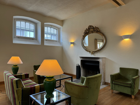 Malteser Kommende - Ansicht Lobby Ein elegantes Wohnzimmer mit stilvollem Kamin, dekorativen Spiegeln und grüner Polstergarnitur.