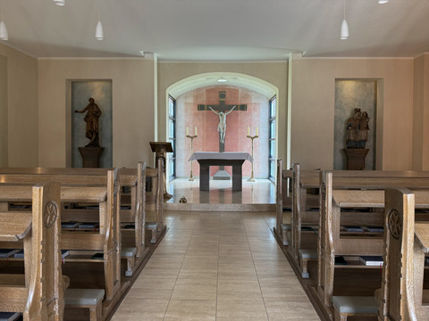 Malteser Kommende - Innenansicht Kapelle <alt>Kirche mit Holzbankreihen, Altar und Kruzifix-Bild im Hintergrund.</alt>