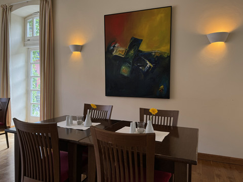Malteser Kommende - Ansicht Lobby  Ein stilvoll dekorierter Esstisch vor einem farbenfrohen abstrakten Gemälde in einem gemütlichen Raum.