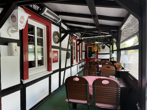Landhaus Orbach Überdachte Terrasse eines Fachwerkhauses mit Holzstühlen und rot-weiß karierten Tischdecken.
