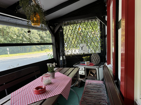 Landhaus Orbach  Gemütliche, rustikale Veranda mit Holzbänken, rot-weißem Tischdecke und Fensterblick ins Grüne.