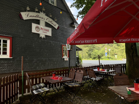 Landhaus Orbach Außenansicht Außenbereich eines traditionellen Gasthauses mit Holztischen und -stühlen unter roten Sonnenschirmen.