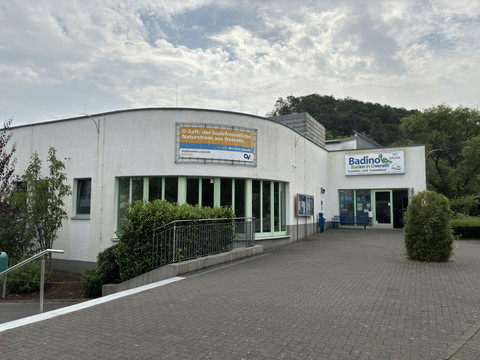 Hallenbad Badino <p>Modernes Freizeitbad mit weißer Fassade in einer grünen Umgebung unter bewölktem Himmel.</p>