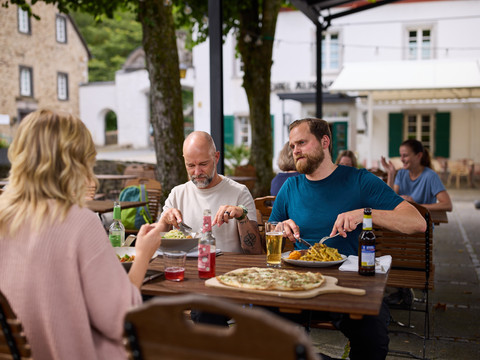 Biergarten Altenberger Hof  Eine Gruppe genießt Essen und Getränke in einem gemütlichen, überdachten Biergarten bei freundlicher Atmosphäre.