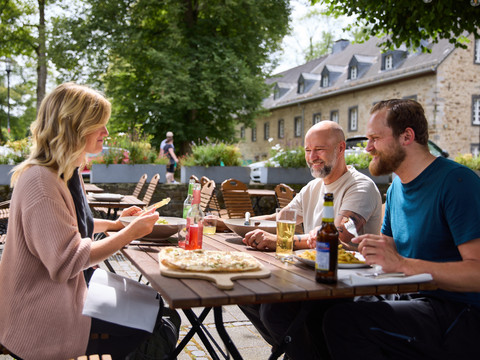 Biergarten Altenberger Hof <p>Menschen genießen Pizza und Drinks auf einer Terrasse vor einem historischen Gebäude in Odenthal.</p>