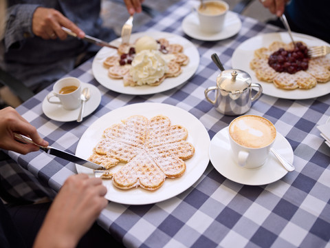 Bergische Waffeln Waffeln mit Puderzucker, Sahne und Kirschen auf gedecktem Tisch mit Kaffee.