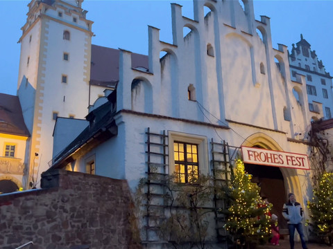 Zusehen ist der Eingang von Schloss Colditz. Am Eingangstor sind zwei geschmückte Weihnachtsbäume aufgestellt und über der Tür hängt ein Banner mit der Aufschrift "Frohes Fest"You can see the entrance to Colditz Castle. Two decorated Christmas trees have been placed at the entrance gate and a banner with the words "Merry Christmas" hangs above the doorMůžete si prohlédnout vstup do hradu Colditz. U vstupní brány jsou umístěny dva ozdobené vánoční stromky a nad dveřmi visí transparent s nápisem "Veselé Vánoce".Widać wejście do zamku Colditz. Przy bramie wejściowej ustawiono dwie udekorowane choinki, a nad drzwiami wisi baner z napisem "Wesołych Świąt".Je kunt de ingang van Kasteel Colditz zien. Twee versierde kerstbomen zijn geplaatst bij de toegangspoort en een spandoek met de woorden "Merry Christmas" (Vrolijk Kerstfeest) hangt boven de deur.Si vede l'ingresso del castello di Colditz. Due alberi di Natale decorati sono stati collocati al cancello d'ingresso e uno striscione con la scritta "Merry Christmas" è appeso sopra la porta.