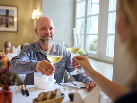 Restaurant Altenberger Hof <p>Ein Paar hebt Weingläser in einem stilvollen Restaurant vor großen Fenstern zum Anstoßen.</p>