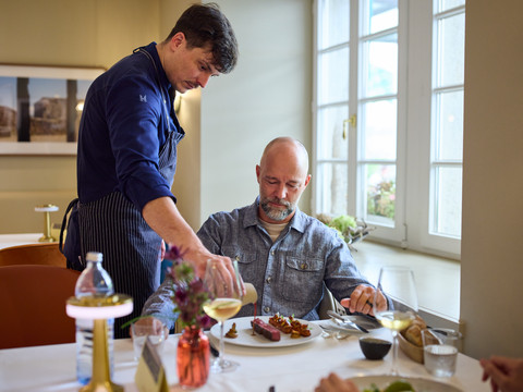 Restaurant Altenberger Hof  Ein Koch serviert einem Gast ein Gourmetgericht in einem stilvoll eingerichteten Restaurant.