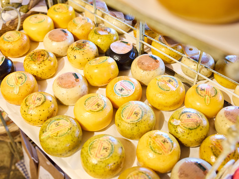 Hofladen Hielscher Hof  <p>Verschiedene Käselaibe in bunten Wachsbeschichtungen liegen auf einem weißen Regal ausgestellt.</p>