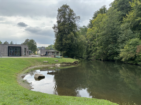 Aggerstrand in Ründeroth Weiher umgeben von Wald in Engelskirchen, mit Spielplatz und modernem Gebäude im Hintergrund.