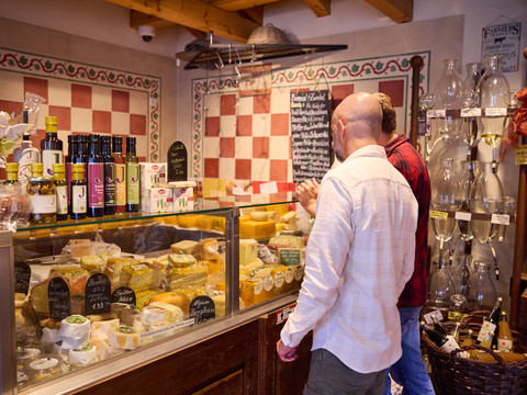 Hofladen Hielscher Hof  Zwei Männer betrachten eine Käsetheke in einem Feinkostgeschäft mit vielfältigen Käsesorten.