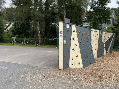 Kletterwand am Aggerstrand Ründeroth Kletterwand im Freien in einem Park in Engelskirchen, umgeben von Bäumen und Fitnessgeräten.