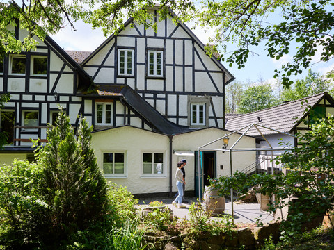 Holsteins Mühle Fachwerkhaus in bewaldeter Umgebung, Person betritt das Gebäude bei sonnigem Wetter.