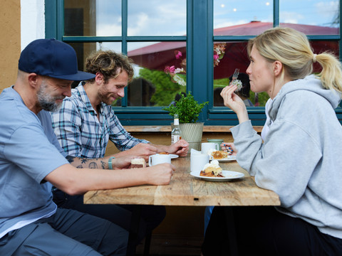 Krewelshof  <p>Drei Personen essen gemütlich an einem Holztisch im Freien bei schönem Wetter.</p>