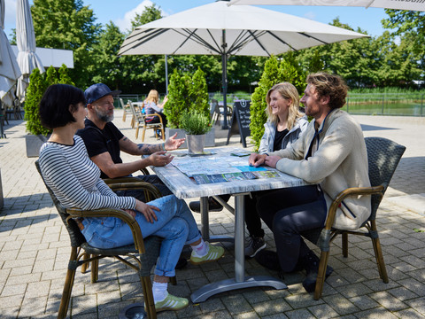 Pause im Biergarten Vier Personen sitzen lachend an einem Gartentisch unter Sonnenschirmen und genießen das Gespräch.