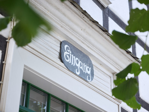 Restaurant Zur Post Eingang eines Fachwerkhauses mit Schild und leicht verdeckten Blättern im Vordergrund.